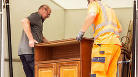 Zwei Männer in Arbeitskleidung verladen ein Möbelstück.